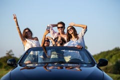 Funny young girls and guys in sunglasses are sitting in a black cabriolet on the road holding their hands up and making royalty free stock photography Funny young girls and guys in sunglasses are sitting in a black cabriolet on the road holding their hands up and making royalty free stock photography