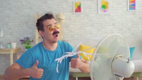 Funny young man in front of a working electric fan escapes from the heat in the apartment slow mo stock video footage Funny young man in front of a working electric fan escapes from the heat in the apartment slow mo stock video footage