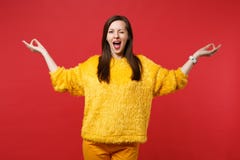 Funny young woman in yellow fur sweater blinking hold hands in yoga gesture keeping mouth wide open isolated on red royalty free stock image Funny young woman in yellow fur sweater blinking hold hands in yoga gesture keeping mouth wide open isolated on red royalty free stock image
