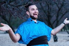 Fuoco selettivo dell'uomo barbuto di risata emozionante nella condizione blu del kimono con le armi stese che guardano awa fotografia stock libera da diritti Fuoco selettivo dell'uomo barbuto di risata emozionante nella condizione blu del kimono con le armi stese che guardano awa fotografia stock libera da diritti