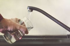 Fyllnads- exponeringsglas med klappvatten Modern vattenkran och vask i hem- kök Man som häller den nya drinken för att kupa royaltyfri fotografi Fyllnads- exponeringsglas med klappvatten Modern vattenkran och vask i hem- kök Man som häller den nya drinken för att kupa royaltyfri fotografi
