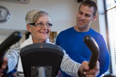 Fysiotherapeut die hogere vrouw helpen bij het uitvoeren van oefening op hometrainer stock afbeelding Fysiotherapeut die hogere vrouw helpen bij het uitvoeren van oefening op hometrainer stock afbeelding