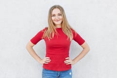 Fêmea contente com cabelo leve e os olhos azuis que têm o sorriso em sua cara que veste a camiseta vermelha e as calças de brim q foto de stock royalty free Fêmea contente com cabelo leve e os olhos azuis que têm o sorriso em sua cara que veste a camiseta vermelha e as calças de brim q foto de stock royalty free