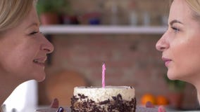Fête des mères, fille avec la maman soufflant la bougie sur le gâteau et souriant étroitement Fête des mères, fille avec la maman soufflant la bougie sur le gâteau et souriant étroitement