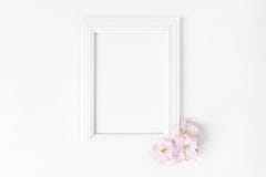 För bildram för vit tom trämodell med rosa japanska körsbärsröda blomningar som ligger på den vita tabellen Affischprodukt royaltyfri bild För bildram för vit tom trämodell med rosa japanska körsbärsröda blomningar som ligger på den vita tabellen Affischprodukt royaltyfri bild