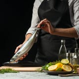 Förberedelse av makrillen av kocken, på en svart bakgrund med citroner, limefrukter royaltyfria bilder Förberedelse av makrillen av kocken, på en svart bakgrund med citroner, limefrukter royaltyfria bilder