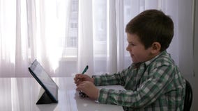 Förskole- utbildning, barnpojke använder minnestavlan för hem- undervisning och gör anmärkningar i anteckningsboken som sitter på lager videofilmer Förskole- utbildning, barnpojke använder minnestavlan för hem- undervisning och gör anmärkningar i anteckningsboken som sitter på lager videofilmer