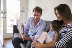 Föräldrar som läser med, behandla som ett barn dottern på Sofa At Home arkivfoton Föräldrar som läser med, behandla som ett barn dottern på Sofa At Home arkivfoton
