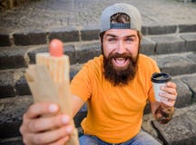 G?odna m??czyzna przek?ska Faceta ?asowania hot dog Obsługuje brodatego kąska smakowitą kiełbasę i pije papierową filiżankę Ulicz obraz stock G?odna m??czyzna przek?ska Faceta ?asowania hot dog Obsługuje brodatego kąska smakowitą kiełbasę i pije papierową filiżankę Ulicz obraz stock