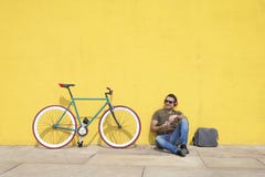 Gafas de sol que llevan del hombre joven que se relajan en el piso y la música que escucha El sentarse contra una pared amarilla imagen de archivo Gafas de sol que llevan del hombre joven que se relajan en el piso y la música que escucha El sentarse contra una pared amarilla imagen de archivo