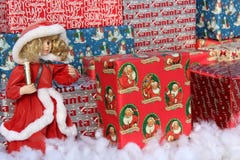 Gaily Wrapped Packages With Dolls Holding Candles At Holiday Event