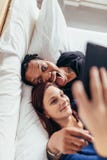 Galna blandras- par som tar selfie på säng royaltyfria bilder Galna blandras- par som tar selfie på säng royaltyfria bilder