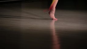 Gambe esili del primo piano dell'atleta della ragazza che esegue gli elementi della ginnastica ritmica con il nastro variopinto Gambe esili del primo piano dell'atleta della ragazza che esegue gli elementi della ginnastica ritmica con il nastro variopinto