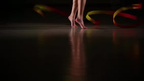 Gambe esili del primo piano dell'atleta della ragazza che esegue gli elementi della ginnastica ritmica con il nastro variopinto Gambe esili del primo piano dell'atleta della ragazza che esegue gli elementi della ginnastica ritmica con il nastro variopinto