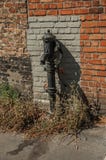 Gammal gatavattenpump som göras i järn som är främst av en tegelstenvägg på staden av Bruges Arkivbilder Gammal gatavattenpump som göras i järn som är främst av en tegelstenvägg på staden av Bruges Arkivbilder