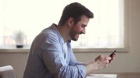 Ganador feliz del hombre joven que usa triunfo móvil de celebración extático del smartphone almacen de video Ganador feliz del hombre joven que usa triunfo móvil de celebración extático del smartphone almacen de video