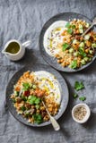 Garbanzos y cuscús condimentados con la ensalada y el yogur griego en un fondo gris, visión superior del ` s del pastor imagenes de archivo Garbanzos y cuscús condimentados con la ensalada y el yogur griego en un fondo gris, visión superior del ` s del pastor imagenes de archivo