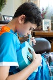 Garçon asiatique de jeune casserole pratiquant sur son ukelele bleu dans un environnement familial photographie stock libre de droits Garçon asiatique de jeune casserole pratiquant sur son ukelele bleu dans un environnement familial photographie stock libre de droits