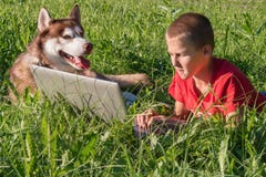 Garçon avec l'ordinateur portable et le chien enroué sur la pelouse verte Enfant et mensonge enroué sibérien rouge côte à côte su photo stock Garçon avec l'ordinateur portable et le chien enroué sur la pelouse verte Enfant et mensonge enroué sibérien rouge côte à côte su photo stock