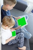 Garçons reposant et à l'aide du comprimé et du téléphone intelligent mobile avec l'écran vert à la maison photographie stock libre de droits Garçons reposant et à l'aide du comprimé et du téléphone intelligent mobile avec l'écran vert à la maison photographie stock libre de droits