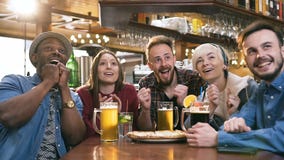 Geconcentreerd vijf jonge vrienden die op voetbalwedstrijd letten terwijl het drinken van bier en cocktail in de bar, bar stock videobeelden Geconcentreerd vijf jonge vrienden die op voetbalwedstrijd letten terwijl het drinken van bier en cocktail in de bar, bar stock videobeelden