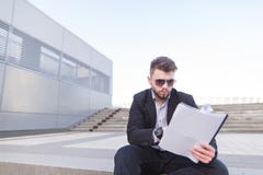 Geconcentreerde bedrijfsmensenzitting op de treden en het bekijken de documenten in zijn handen stock fotografie Geconcentreerde bedrijfsmensenzitting op de treden en het bekijken de documenten in zijn handen stock fotografie