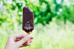 Gelato del cioccolato nella glassa del cioccolato su un bastone in una mano femminile su un fondo verde fotografie stock libere da diritti Gelato del cioccolato nella glassa del cioccolato su un bastone in una mano femminile su un fondo verde fotografie stock libere da diritti