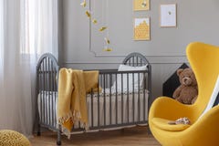 Gele stoel en, bruine teddybeer en grijze houten voederbak met deken in elegante babyslaapkamer royalty-vrije stock foto Gele stoel en, bruine teddybeer en grijze houten voederbak met deken in elegante babyslaapkamer royalty-vrije stock foto
