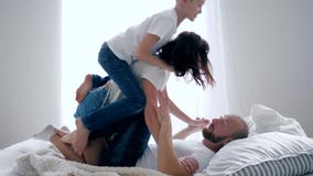Gelukkige familie in identieke witte T-shirts die samen prettijd, jongen met zijn moeder hebben die op vader op bed springen stock footage Gelukkige familie in identieke witte T-shirts die samen prettijd, jongen met zijn moeder hebben die op vader op bed springen stock footage