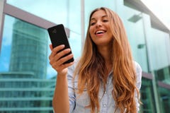 Gelukkige glimlachende vrouw die in bedrijfsdistrict lopen die een smartphone gebruiken Lage hoek royalty-vrije stock fotografie Gelukkige glimlachende vrouw die in bedrijfsdistrict lopen die een smartphone gebruiken Lage hoek royalty-vrije stock fotografie