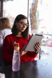Gelukkige jonge vrouw het drinken limonade/bevroren thee en het gebruiken van tabletcomputer in een koffiewinkel stock fotografie Gelukkige jonge vrouw het drinken limonade/bevroren thee en het gebruiken van tabletcomputer in een koffiewinkel stock fotografie