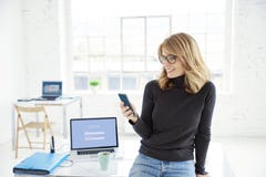 Gelukkige onderneemster die met somebody op haar mobiele telefoon spreken terwijl status in het bureau royalty-vrije stock afbeeldingen Gelukkige onderneemster die met somebody op haar mobiele telefoon spreken terwijl status in het bureau royalty-vrije stock afbeeldingen