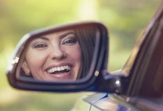 Gelukkige vrouwenbestuurder die in de spiegel van het auto zijaanzicht het lachen kijken royalty-vrije stock fotografie Gelukkige vrouwenbestuurder die in de spiegel van het auto zijaanzicht het lachen kijken royalty-vrije stock fotografie