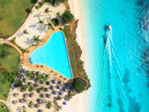 Aerial view of pool, sandy beach, palms, umbrellas, boat, sea