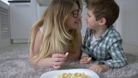 Gente hambrienta, niño agradable con la madre que come los dulces que mienten en piso en casa almacen de video Gente hambrienta, niño agradable con la madre que come los dulces que mienten en piso en casa almacen de video