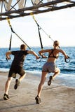 Gente juguetona joven que entrena con el trx cerca del mar por la mañana Fotos de archivo Gente juguetona joven que entrena con el trx cerca del mar por la mañana Fotos de archivo