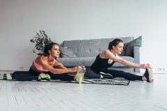Geschikte vrouwen die het uitrekken doen zich terwijl thuis het zitten op de vloer stock afbeelding Geschikte vrouwen die het uitrekken doen zich terwijl thuis het zitten op de vloer stock afbeelding