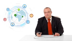 Geschäftsmann, der am Schreibtisch sitzt und ein Mobiltelefon mit Kugel hält Stockfotografie Geschäftsmann, der am Schreibtisch sitzt und ein Mobiltelefon mit Kugel hält Stockfotografie