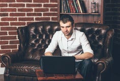 Geschäftsmann sitzt auf einem ledernen Sofa hinter einem Laptop auf dem Hintergrund des Rauminnenraums Ein Mann arbeitet in eigen lizenzfreie stockbilder Geschäftsmann sitzt auf einem ledernen Sofa hinter einem Laptop auf dem Hintergrund des Rauminnenraums Ein Mann arbeitet in eigen lizenzfreie stockbilder