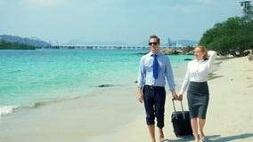 Geschäftsmann und Geschäftsfrau mit einem Koffer gehend entlang den weißen Sandstrand auf der Insel stockfoto Geschäftsmann und Geschäftsfrau mit einem Koffer gehend entlang den weißen Sandstrand auf der Insel stockfoto