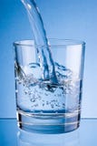 Gietend water in glas op blauwe achtergrond royalty-vrije stock foto Gietend water in glas op blauwe achtergrond royalty-vrije stock foto