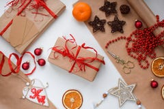 A gift in craft paper tied with a red ribbon surrounded by Christmas trivia, balls, garlands, dried oranges, wooden toys stock photos A gift in craft paper tied with a red ribbon surrounded by Christmas trivia, balls, garlands, dried oranges, wooden toys stock photos