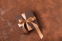 A gift in a paper box is decorated with a satin ribbon and a bow on a brown background. Festive concept.Flat layout. stock image A gift in a paper box is decorated with a satin ribbon and a bow on a brown background. Festive concept.Flat layout. stock image