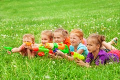 Gioco dei bambini con le pistole a acqua che mettono su un prato immagini stock libere da diritti Gioco dei bambini con le pistole a acqua che mettono su un prato immagini stock libere da diritti