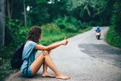 Giovane bella donna che fa auto-stop seduta sulla strada immagine stock Giovane bella donna che fa auto-stop seduta sulla strada immagine stock