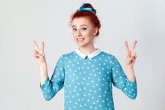 Giovane bella ragazza della testarossa con il vestito blu e la banda capa che mostrano il segno di pace fotografia stock libera da diritti Giovane bella ragazza della testarossa con il vestito blu e la banda capa che mostrano il segno di pace fotografia stock libera da diritti
