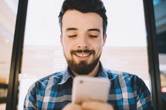 Giovane bello allegro che per mezzo del suo smartphone per la chiacchierata con gli amici fotografie stock Giovane bello allegro che per mezzo del suo smartphone per la chiacchierata con gli amici fotografie stock