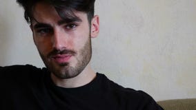 Giovane bello che si siede sullo strato Giovane bello che si siede sullo strato