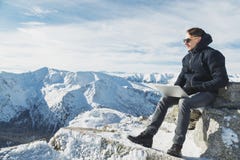 Giovane blogger o free lance che lavora ad un computer portatile sopra il mondo Lanscape di inverno nel giorno soleggiato immagine stock Giovane blogger o free lance che lavora ad un computer portatile sopra il mondo Lanscape di inverno nel giorno soleggiato immagine stock