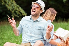 Giovane chegode dell'ascoltare la sua canzone favorita Sedendosi di nuovo alla parte posteriore con la sua amica che sta leggendo fotografia stock Giovane chegode dell'ascoltare la sua canzone favorita Sedendosi di nuovo alla parte posteriore con la sua amica che sta leggendo fotografia stock